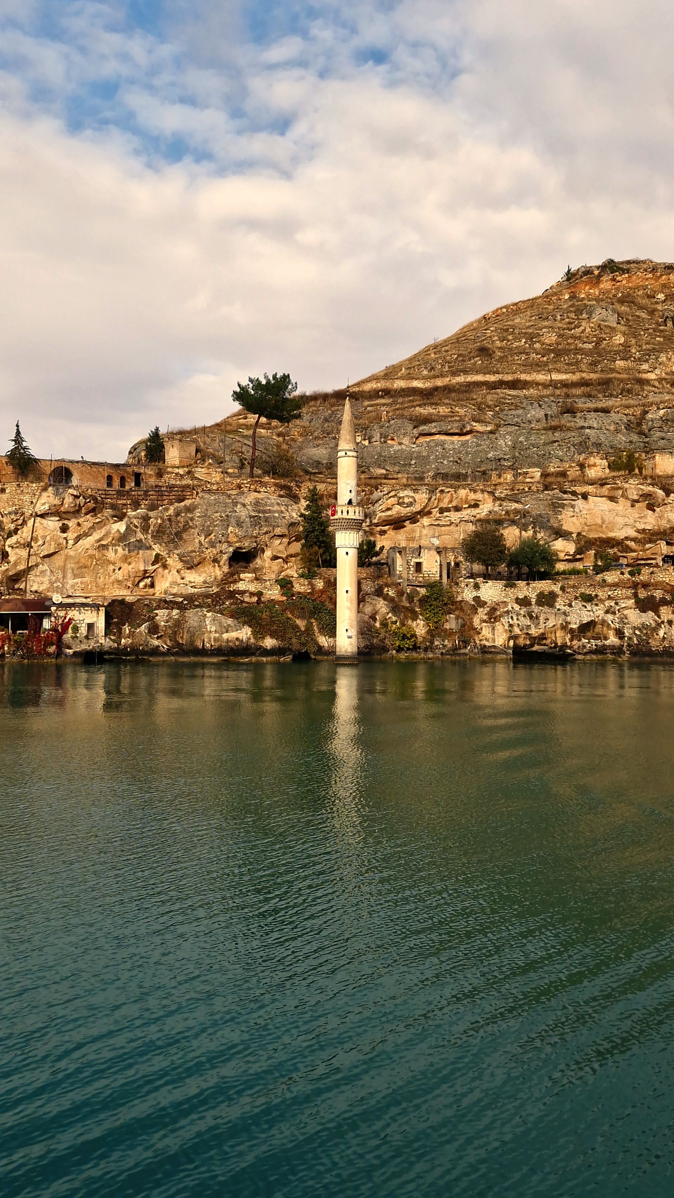 Scenic view of a lone minaret by rocky cliffs reflected in a tranquil lake.