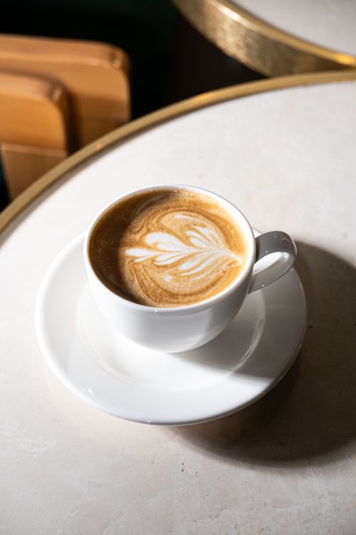 Free A cappuccino with intricate latte art served in a white cup on a sunlit tabletop. Stock Photo