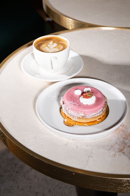 Delicious pink pastry and frothy latte on an elegant marble table setting.