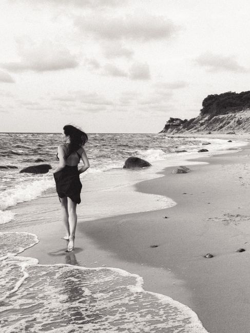 Woman walking along a secluded beach under cloudy skies, capturing a moment of solitude.