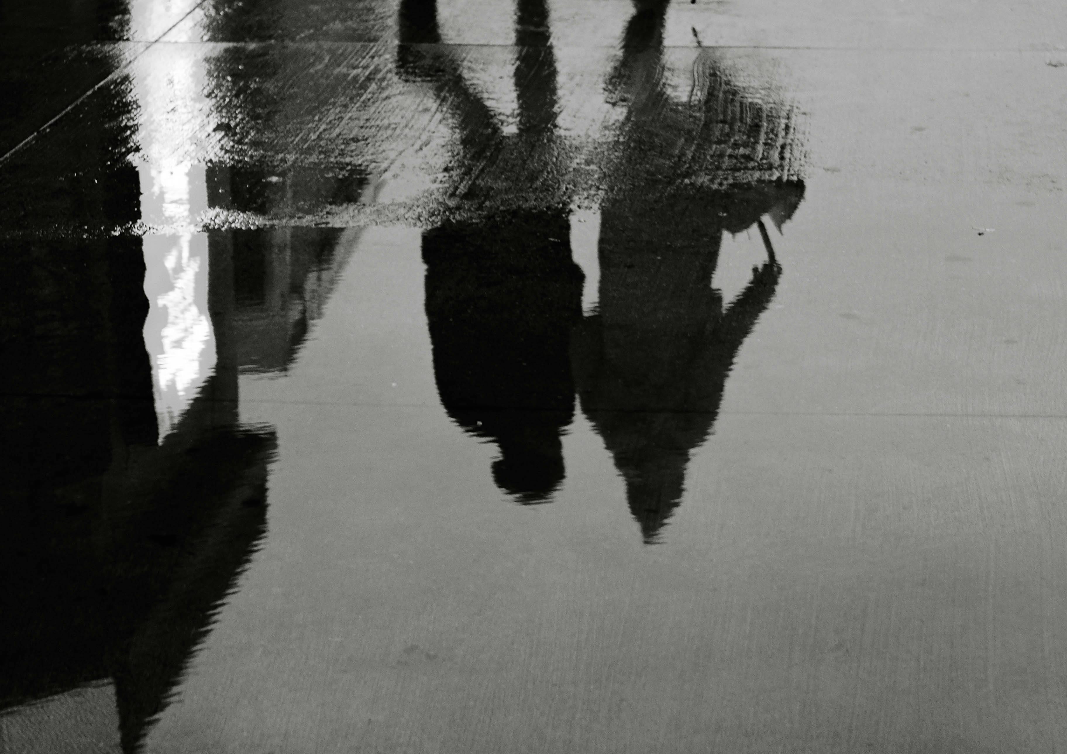Gratuit Reflecții cu siluetă a doi oameni pe pavajul umed în timpul unei zile ploioase. Fotografie de stoc