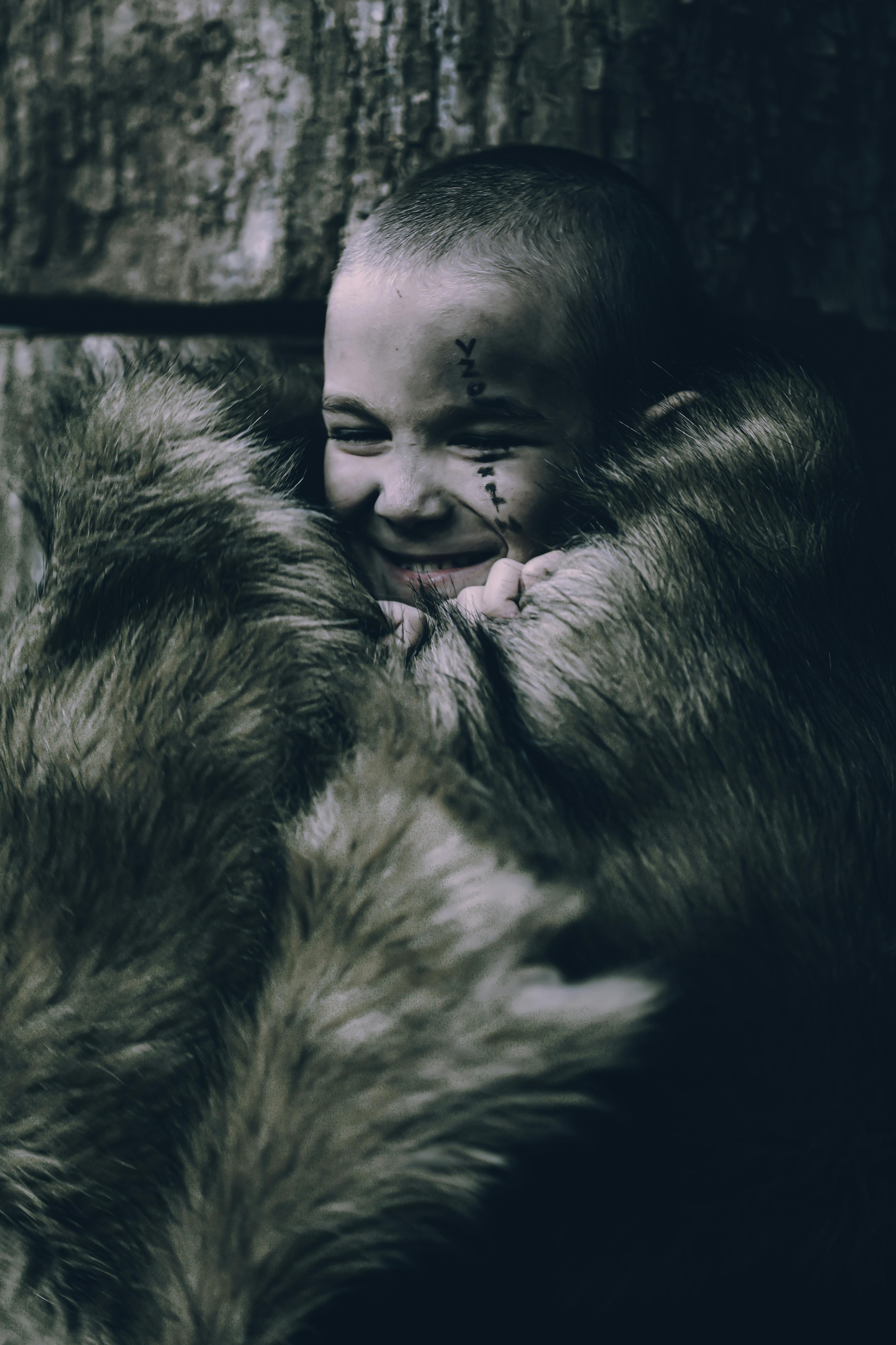 A child wrapped in a fur blanket showing tribal face paint, expressing joy.
