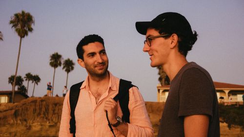 Free Two friends chatting outdoors at sunset, creating a warm and relaxed atmosphere. Stock Photo