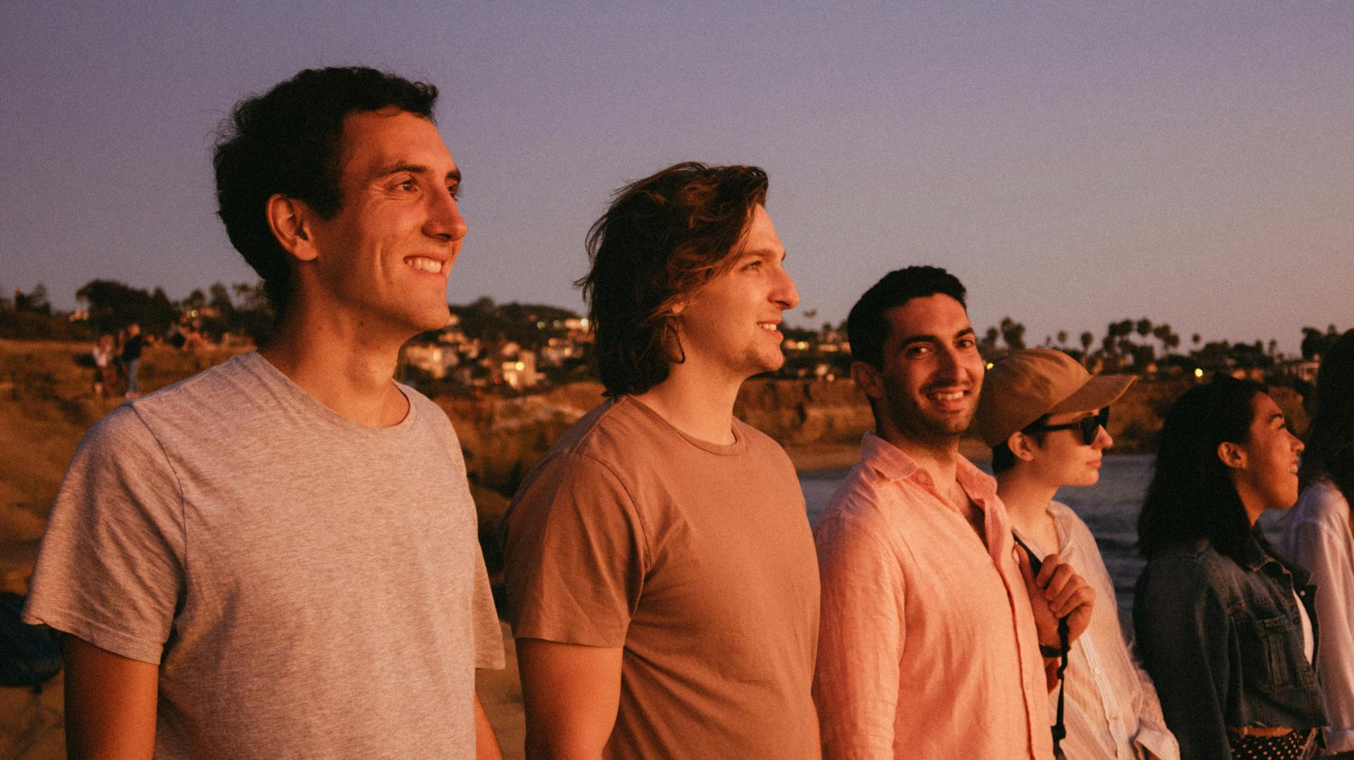 A group of friends watching the sunset at the beach, smiling and enjoying the summer evening.