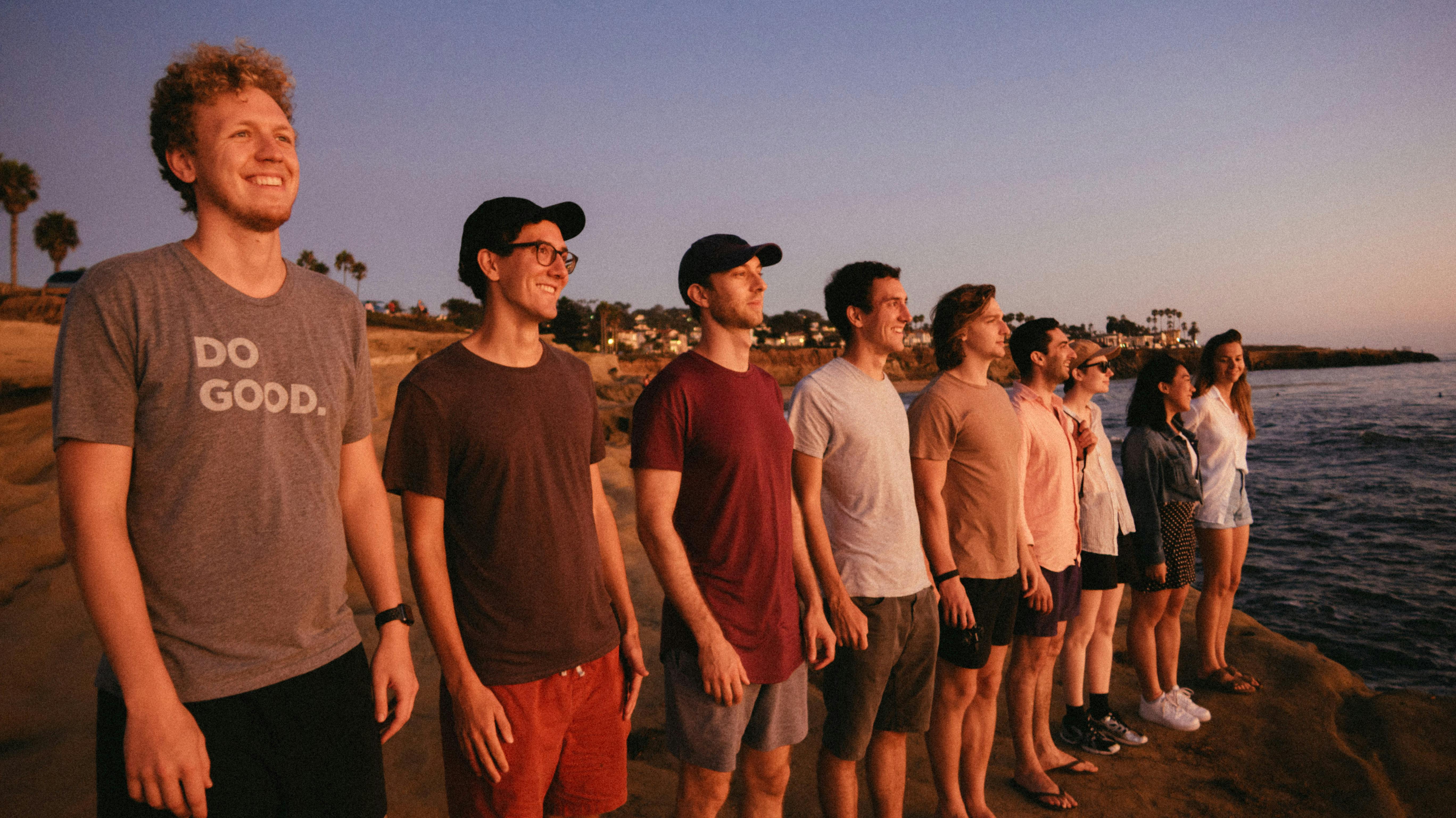 A group of friends smiling at the sunset by the rocky seaside.