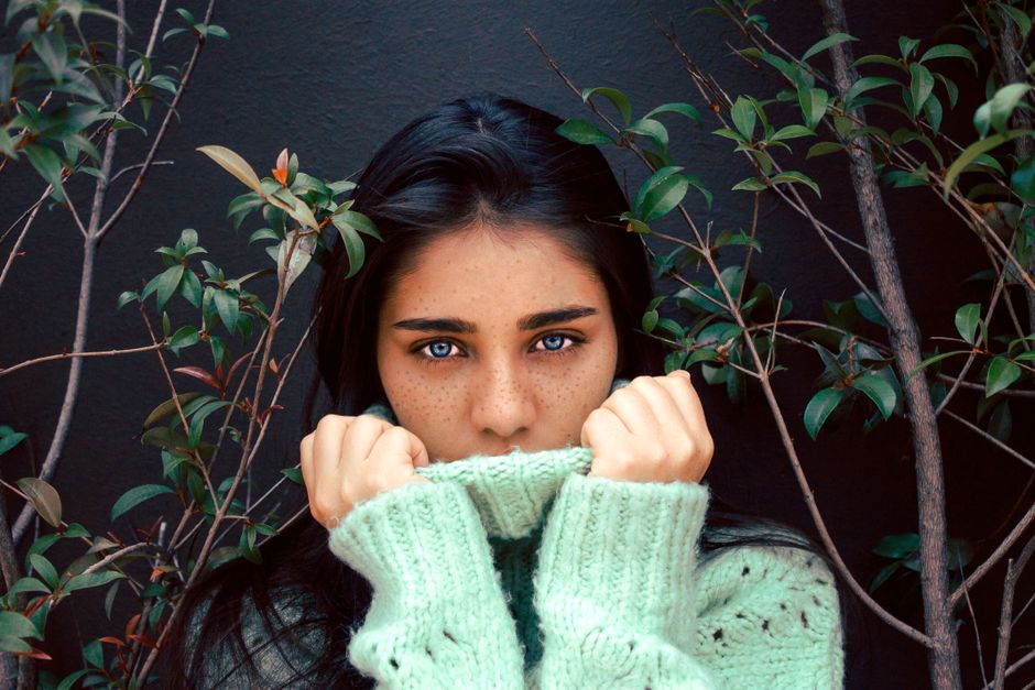 A captivating portrait of a woman with freckles and blue eyes surrounded by leaves.