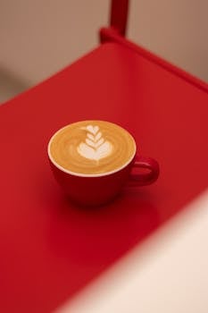 A beautifully crafted latte art in a red cup on a stylish red table, perfect for coffee enthusiasts.
