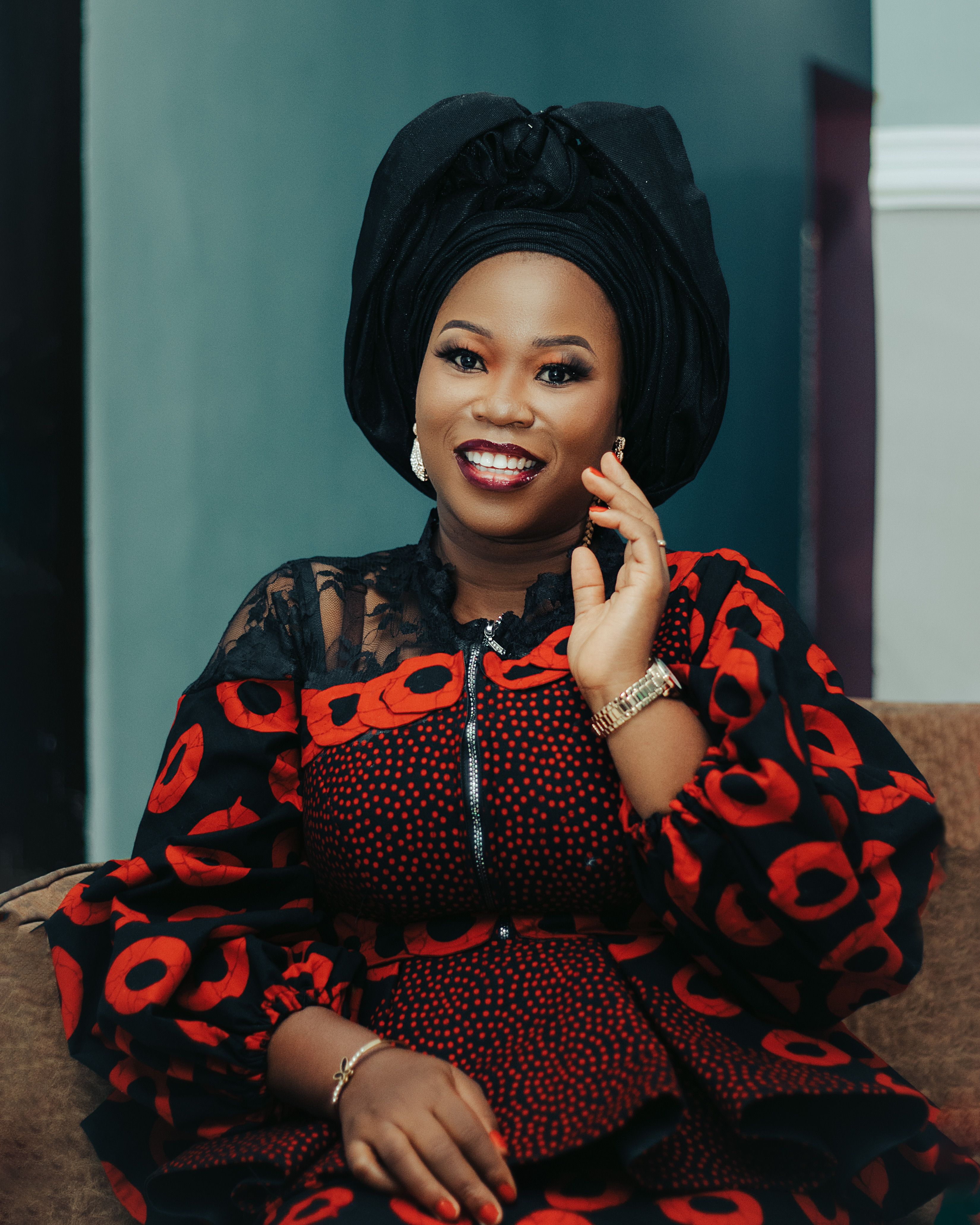 Portrait of a smiling woman in vibrant African attire and headwrap, posing indoors.