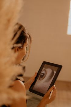 A woman uses a tablet and stylus for photo editing in a warmly lit room.