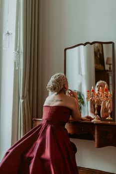 A woman in a red dress applies lipstick in front of a vintage mirror, enhancing her elegance.