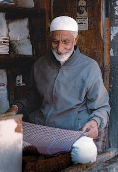 Elderly man skillfully working on fabric in a rustic workshop, showcasing traditional craftsmanship.