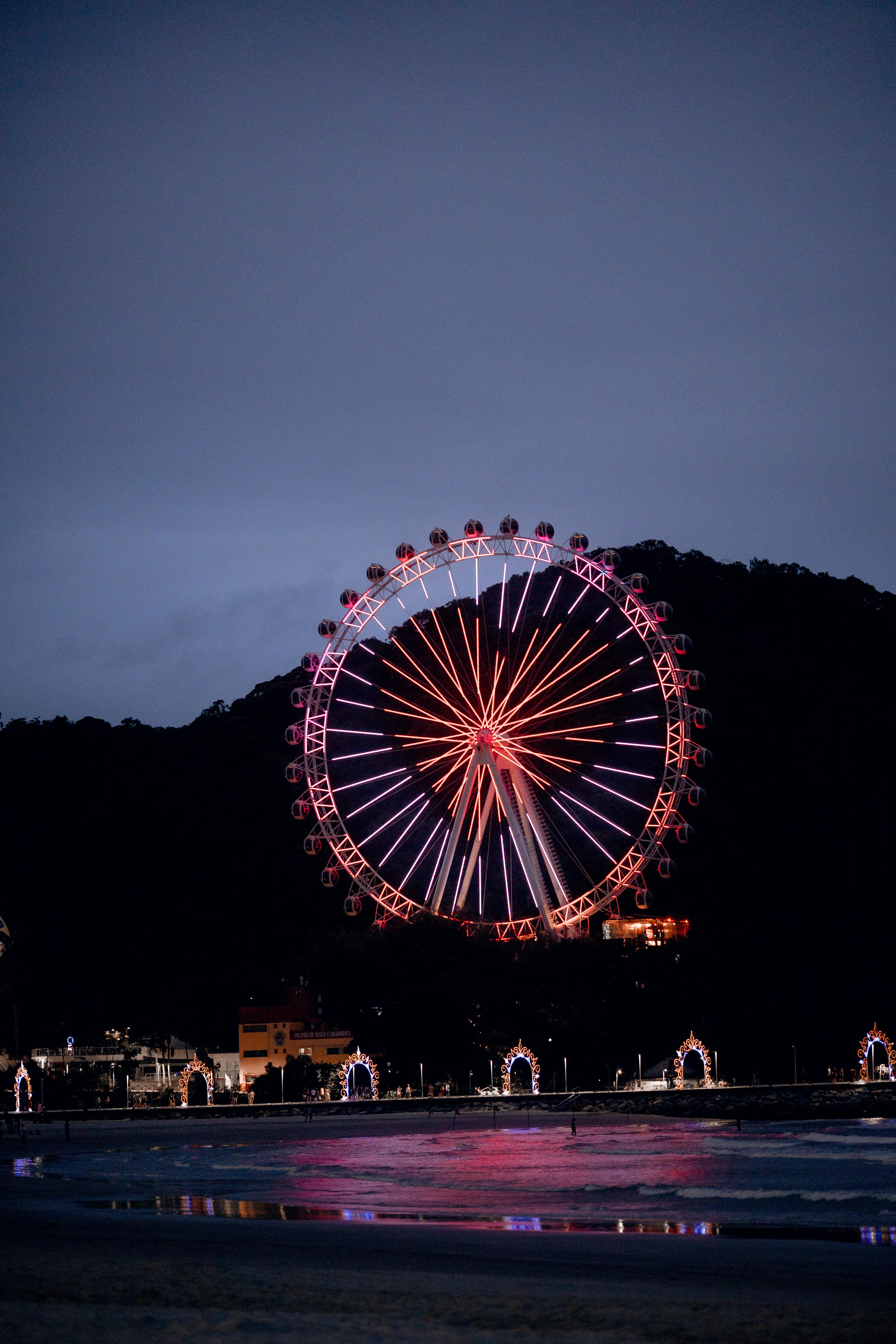 Illuminated ferris wheel at night against a dark sky reflecting on water.