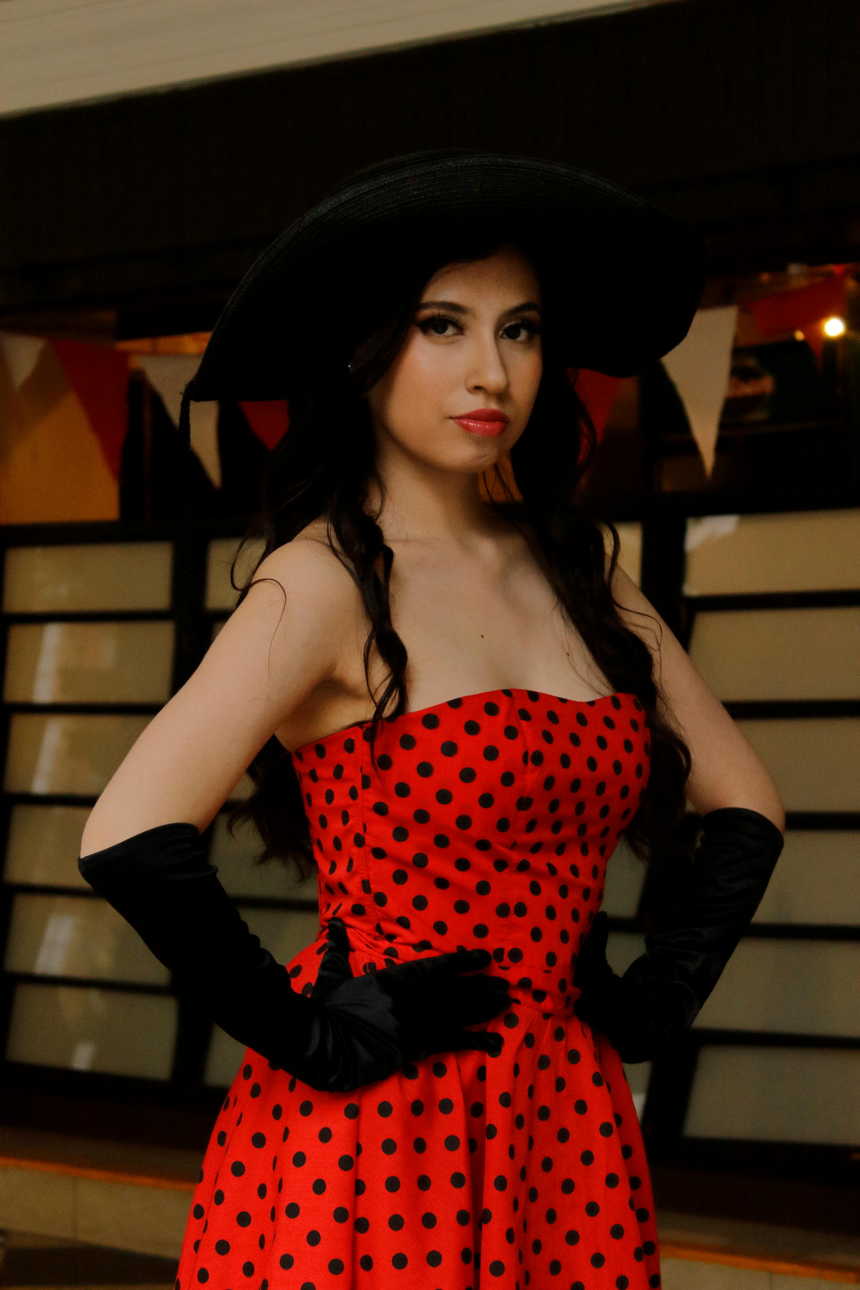 Stylish woman in a red polka dot dress with black gloves and hat, exuding vintage elegance.