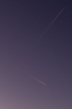 Twilight sky featuring intersecting airplane contrails forming a cross pattern against a gradient background.