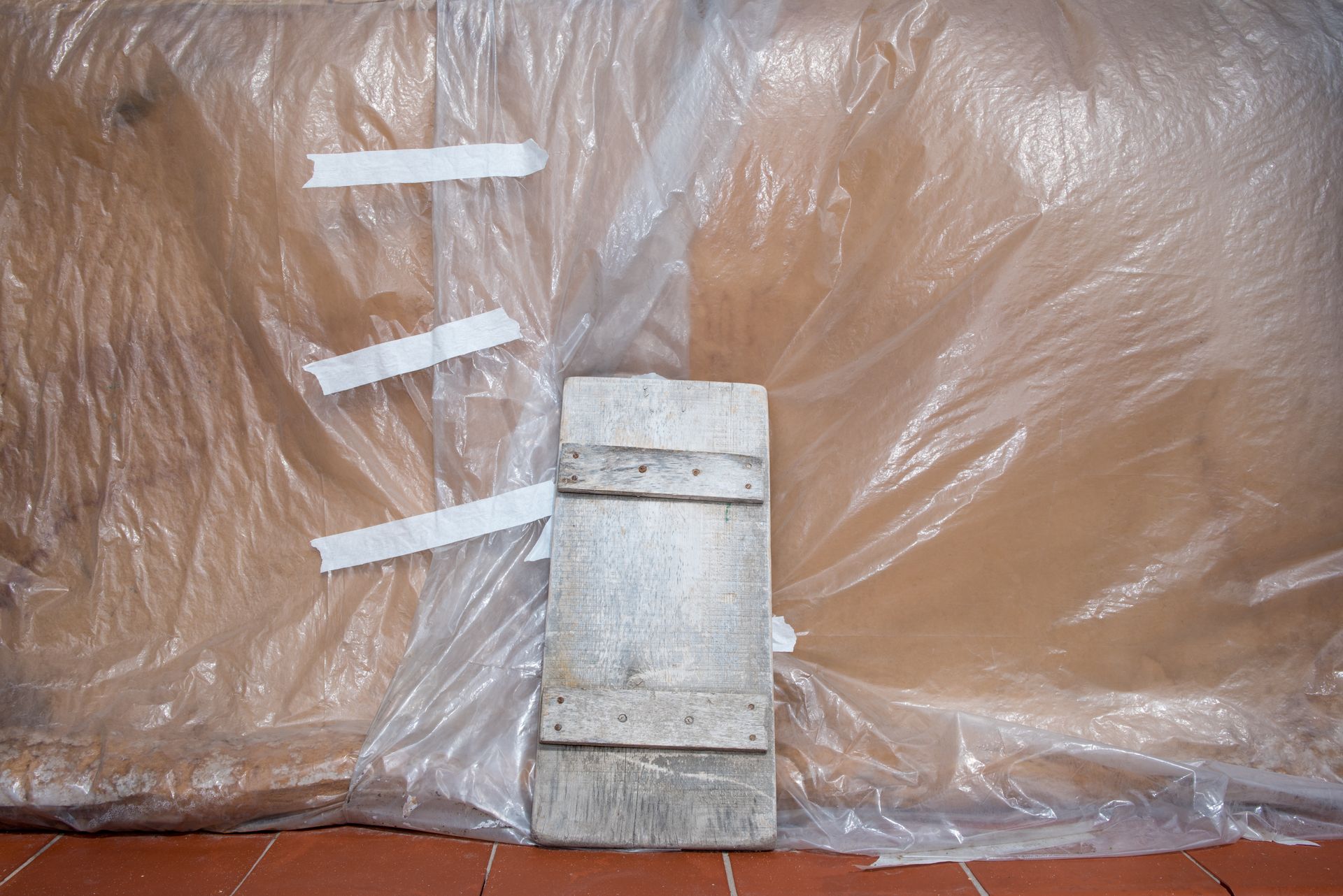 Plastic tarp with wooden board and tape indoors, showcasing rustic industrial setup.