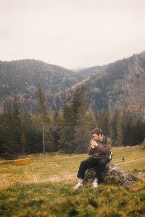 Free A man sits on a rock, smoking, surrounded by mountains and trees. Stock Photo