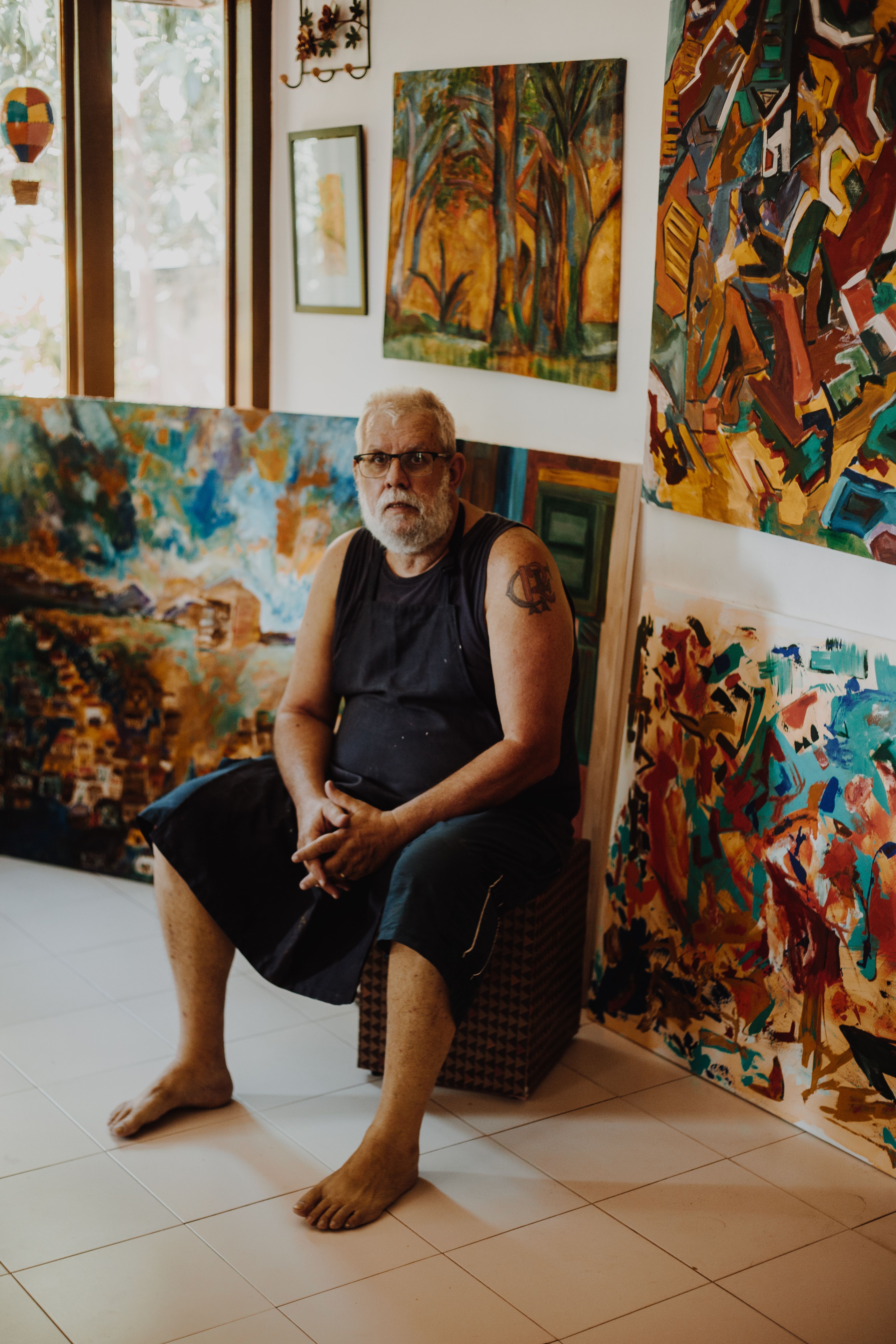 Portrait of a Brazilian artist surrounded by colorful paintings in his studio.