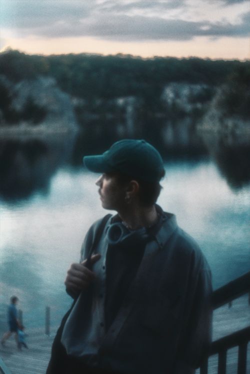 Free A teenager gazes across a calm lake during twilight, creating a moody atmosphere. Stock Photo