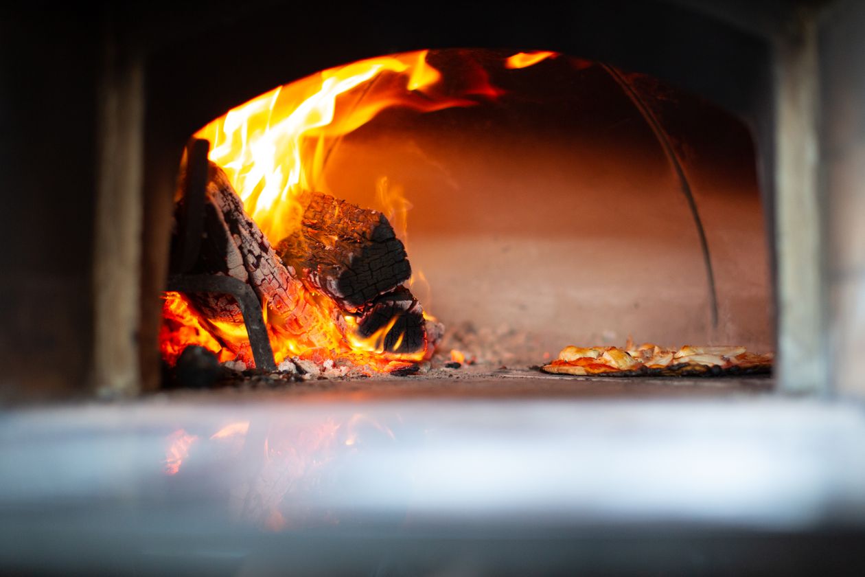 Flames and glowing coals inside a wood-fired pizza oven with a pizza cooking on the stone