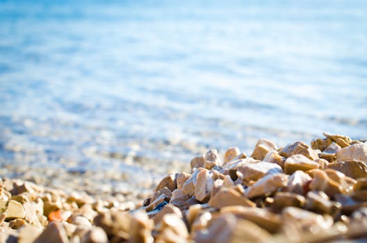 阳光明媚的海滩上，鹅卵石散落在平静清澈的大海边，非常适合夏日氛围