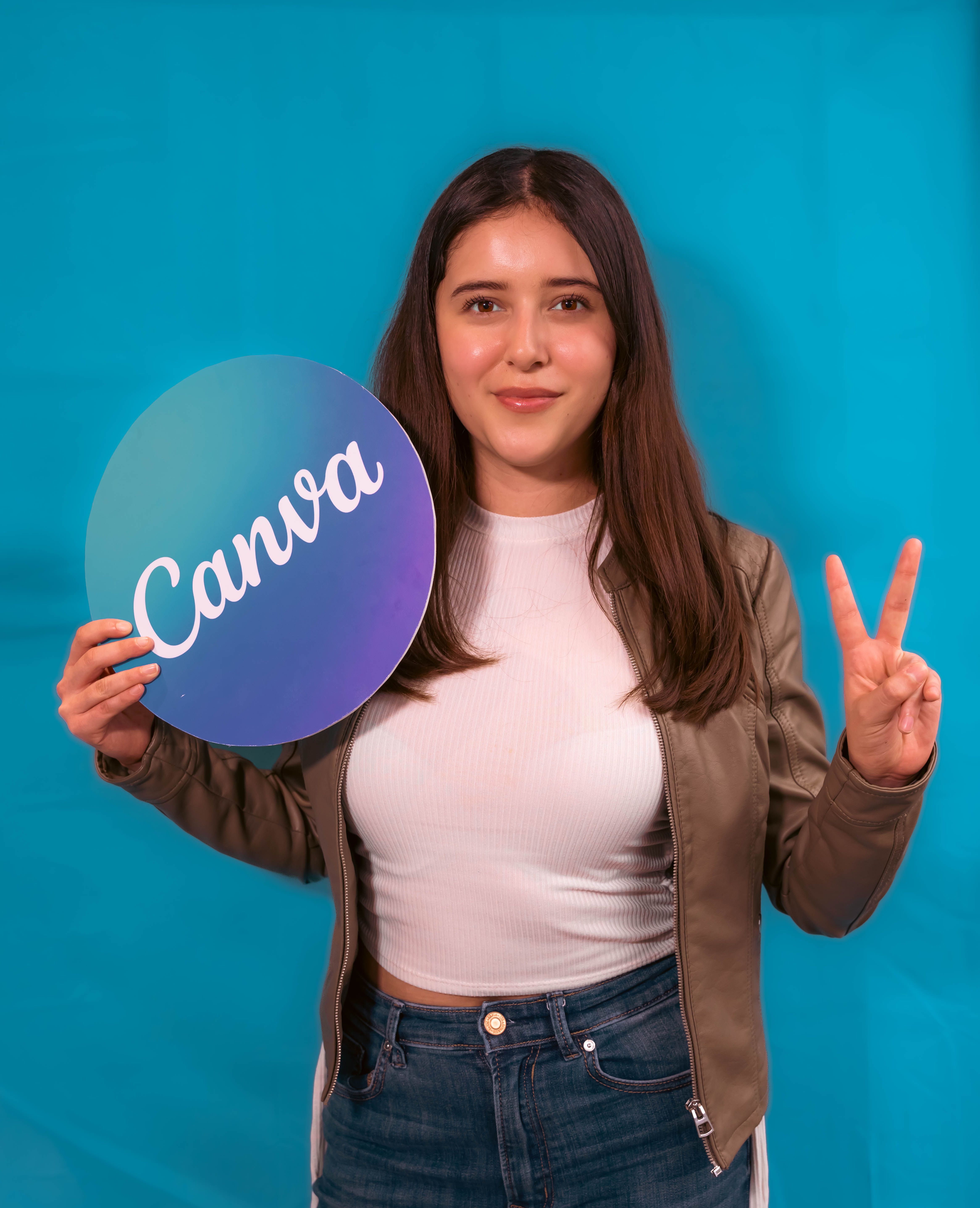 Confident young woman holding a round sign against a vibrant blue backdrop.