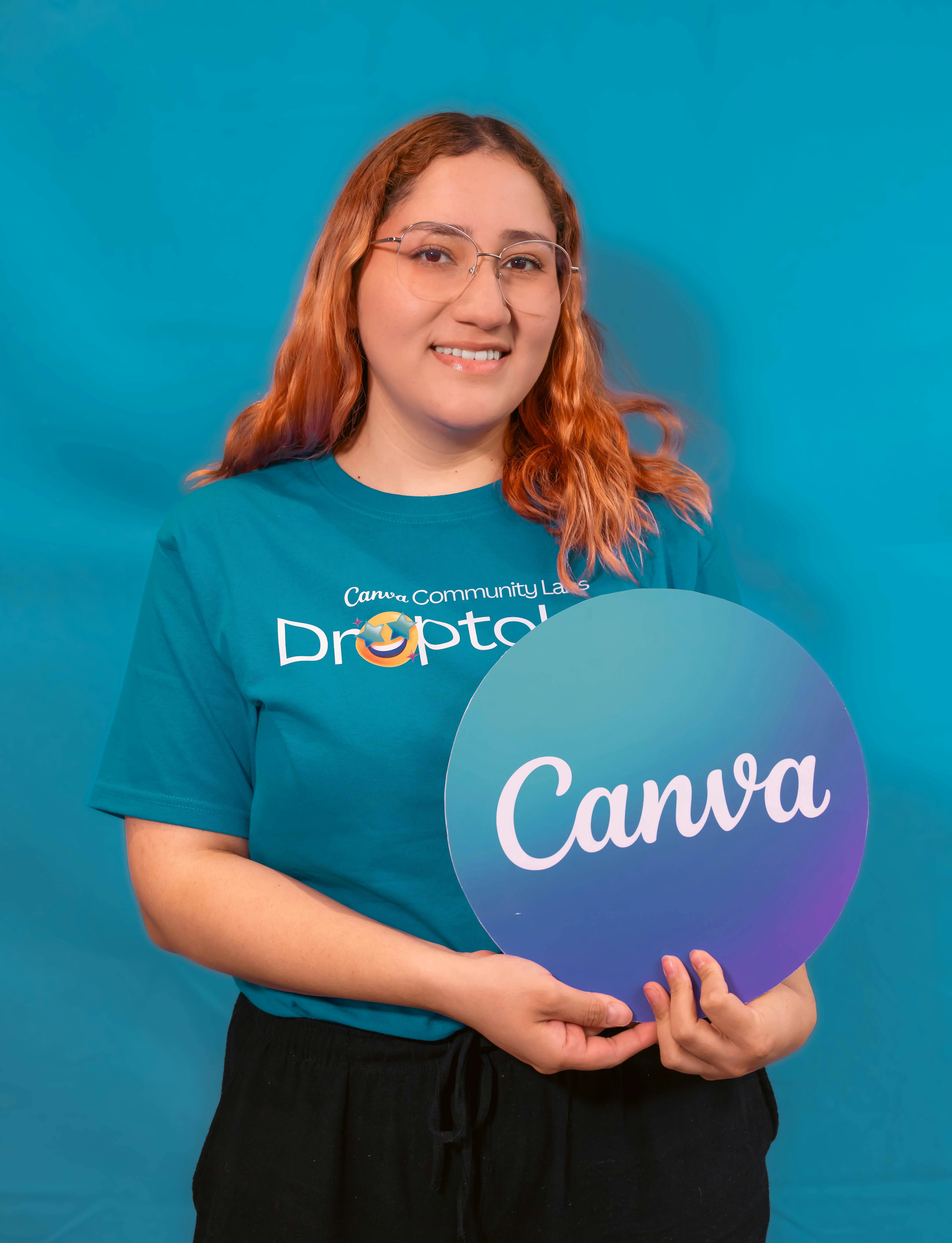 Smiling woman in Canva t-shirt holding brand logo sign, with blue backdrop.
