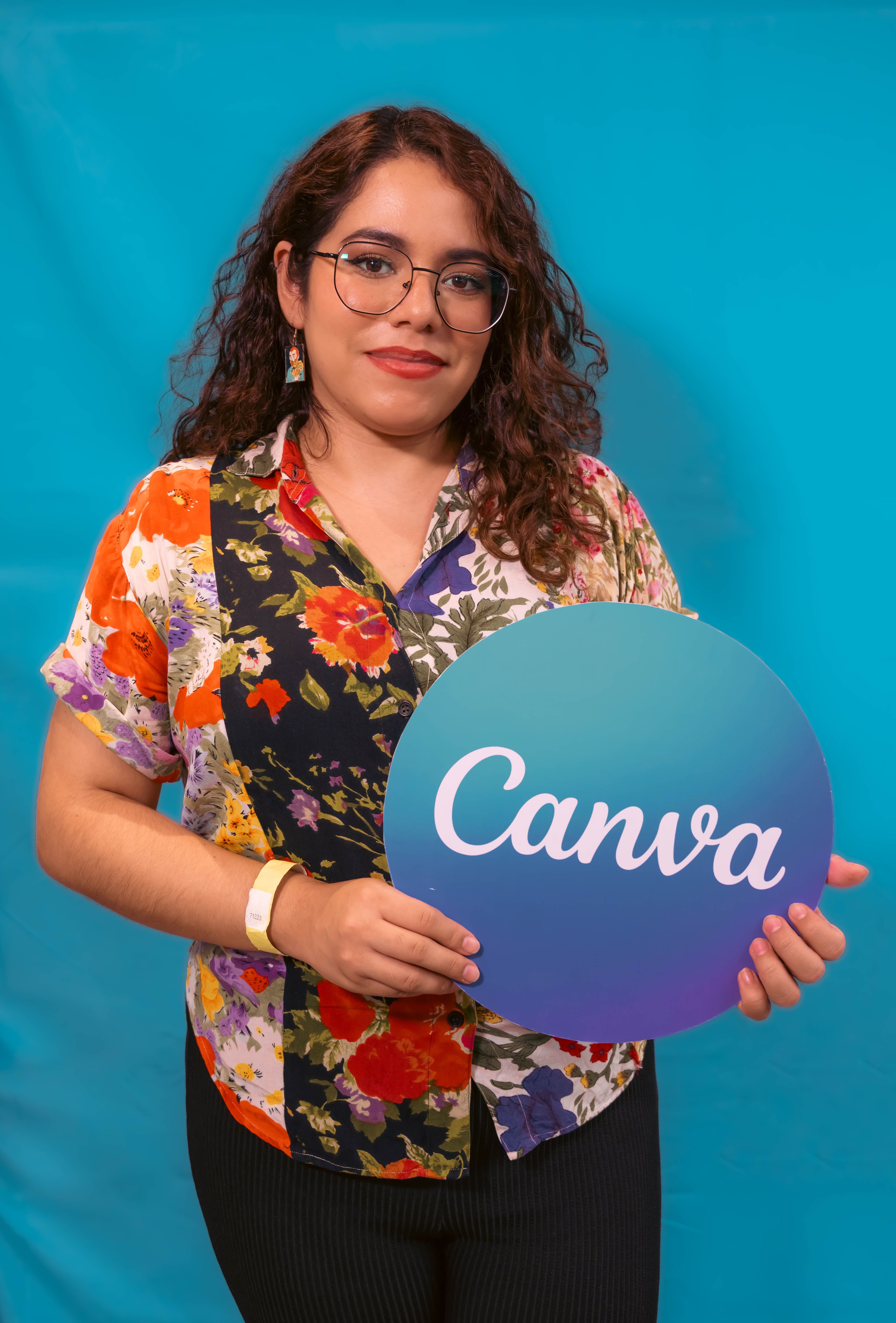 Smiling woman with floral shirt holding a Canva logo sign against a blue backdrop.