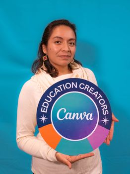 Portrait of a woman holding an Education Creators sign against a blue background.