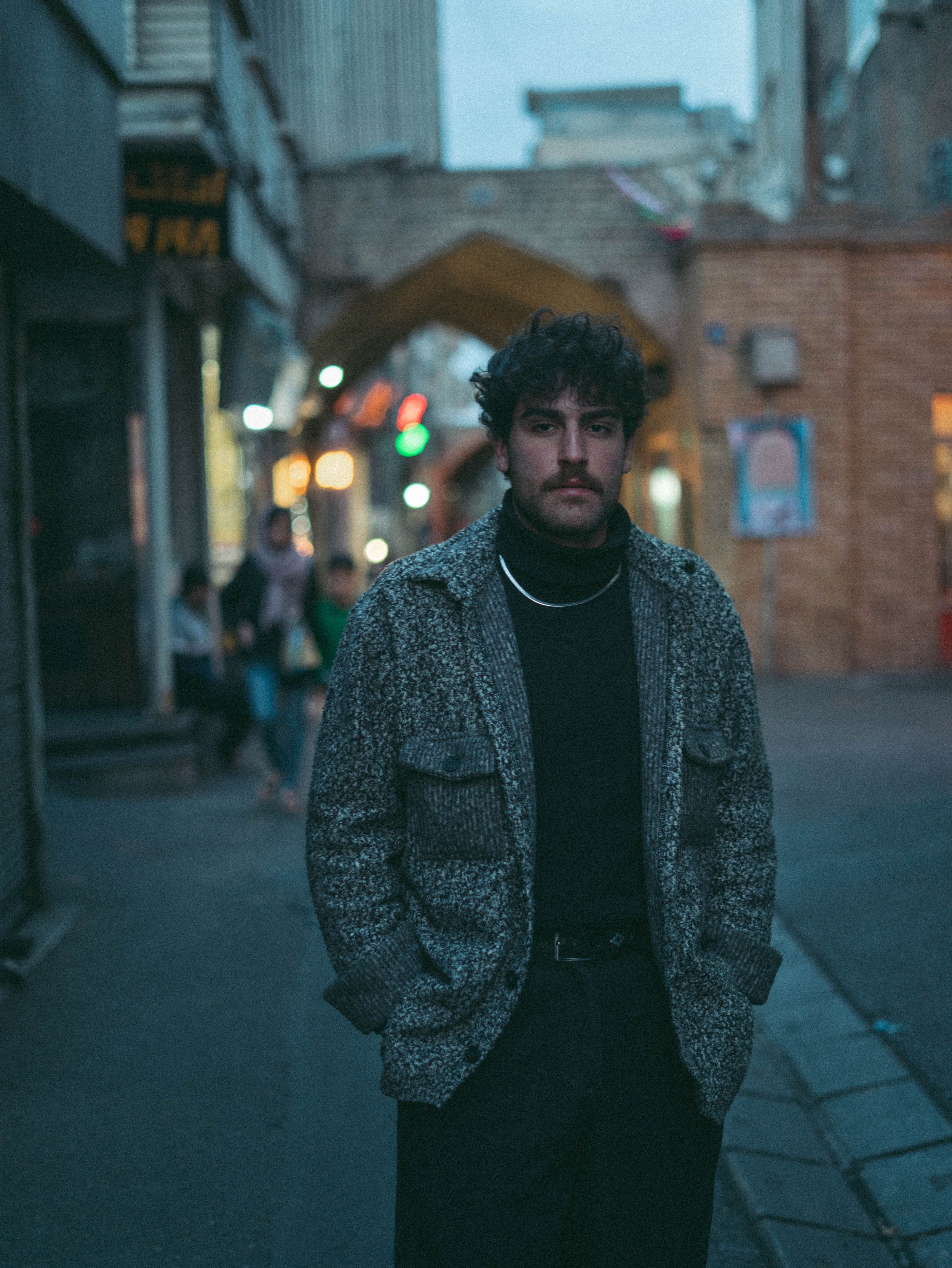 Man standing on a city street during evening time, surrounded by urban lights.