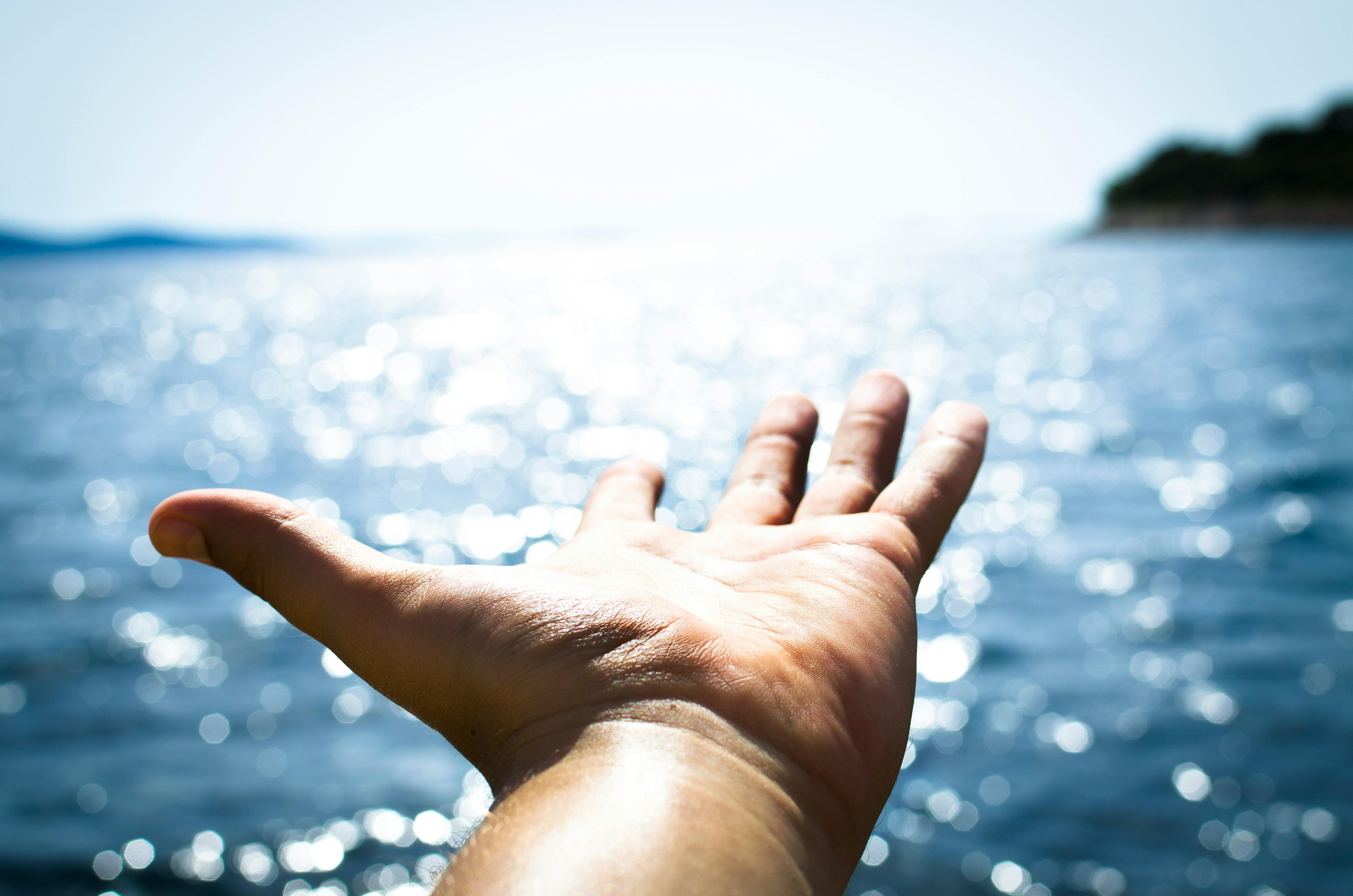 Person Hand Reaching Body of Water · Free Stock Photo