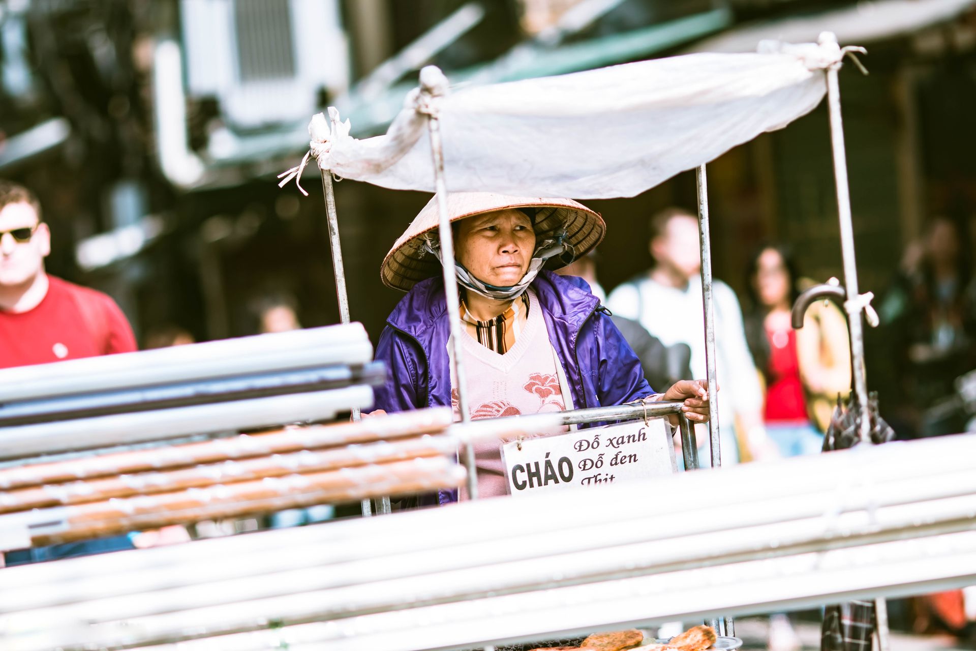 Vietnamese street vendor in Hanoi market selling traditional food from a cart.
