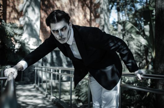 A striking gothic-themed portrait of a male model outdoors with intense shadows.