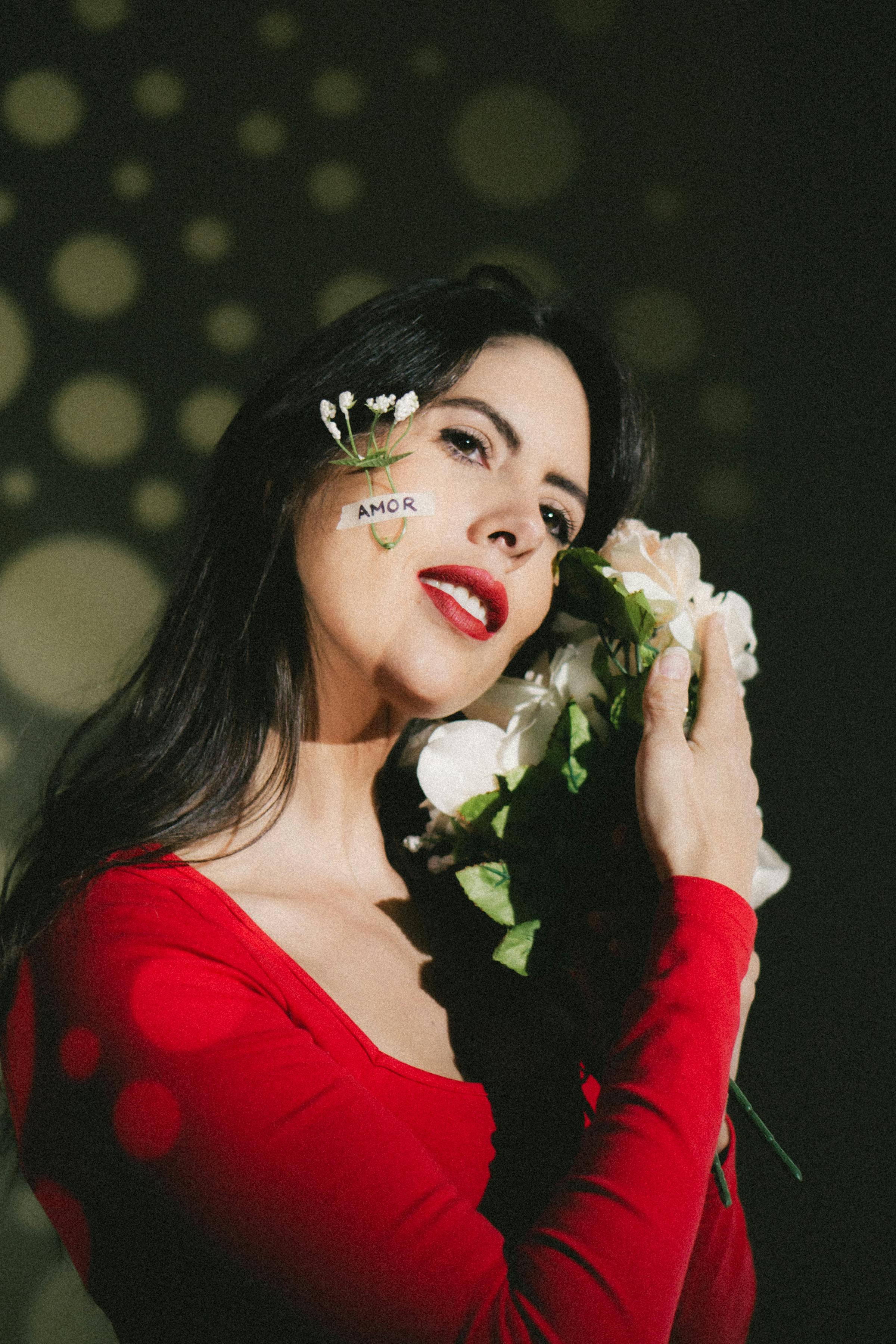 Woman in red embraces white flowers with 'amor' written on face, exuding love and warmth.