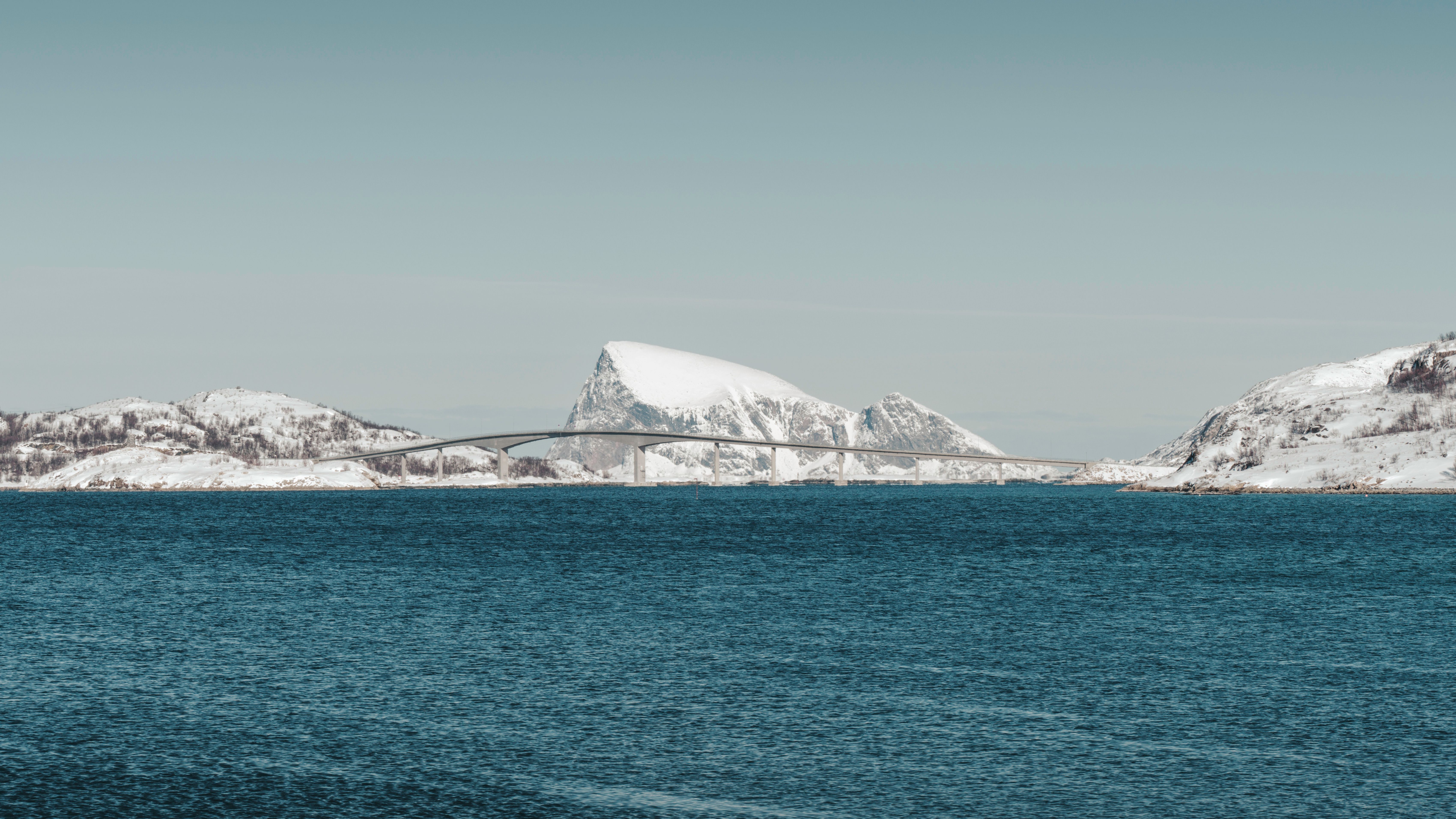 Serene winter landscape featuring a bridge over icy waters with snow-covered mountains in Northern Norway.