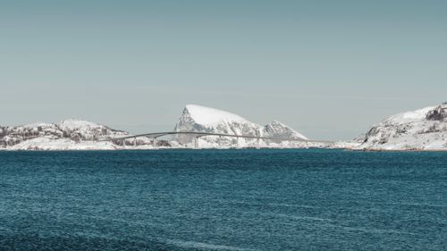 Free Serene winter landscape featuring a bridge over icy waters with snow-covered mountains in Northern Norway. Stock Photo