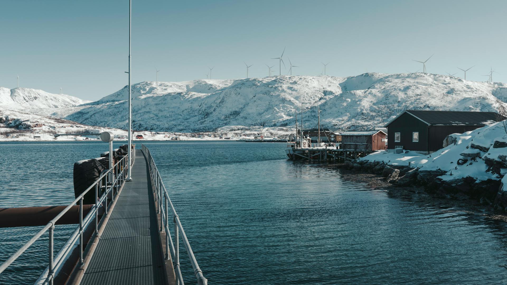 Scenic snowy fjord in Northern Norway with wind turbines and calm waters.