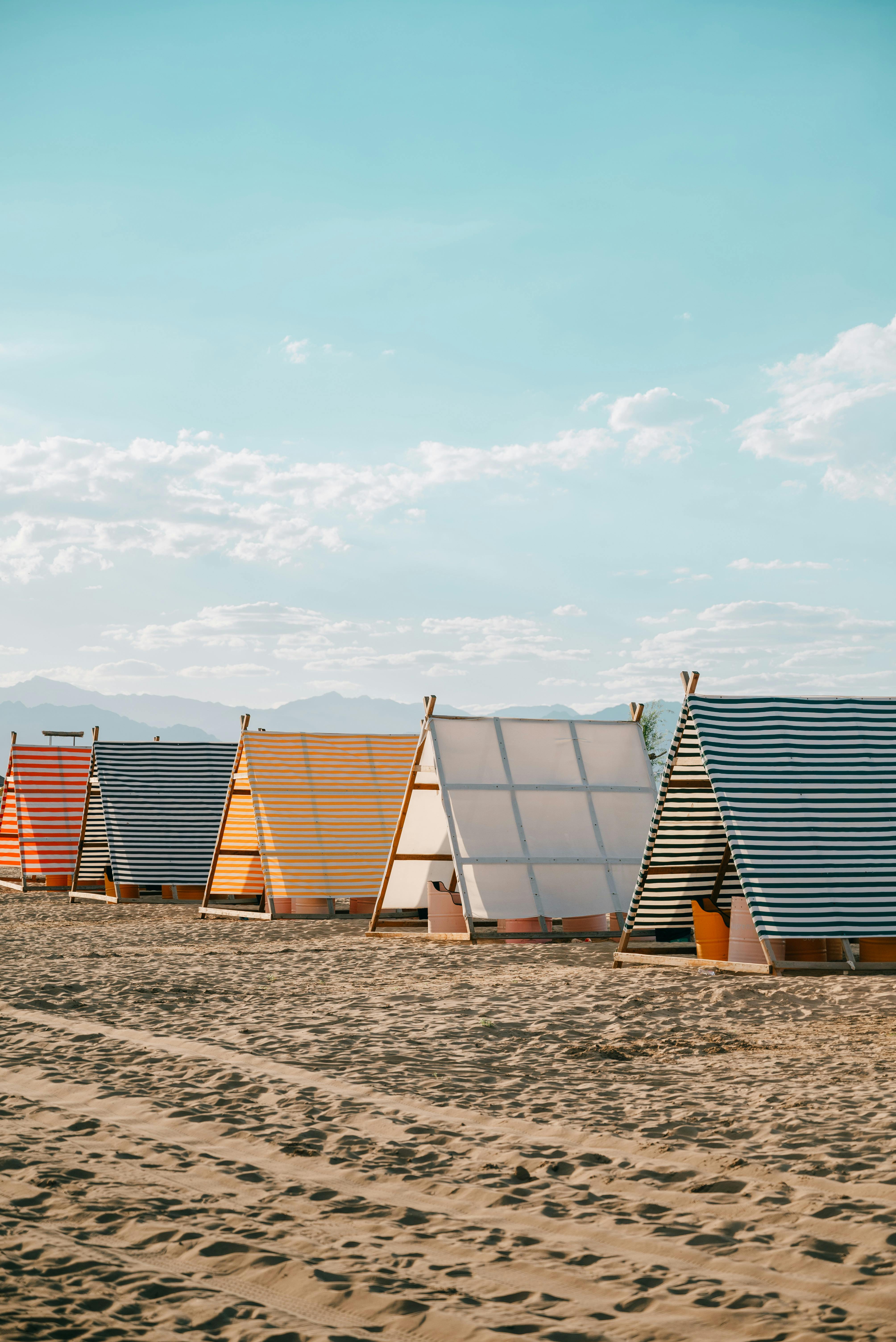 Striped beach tents lined up on a sunny sandy shore with vibrant hues and clear sky.