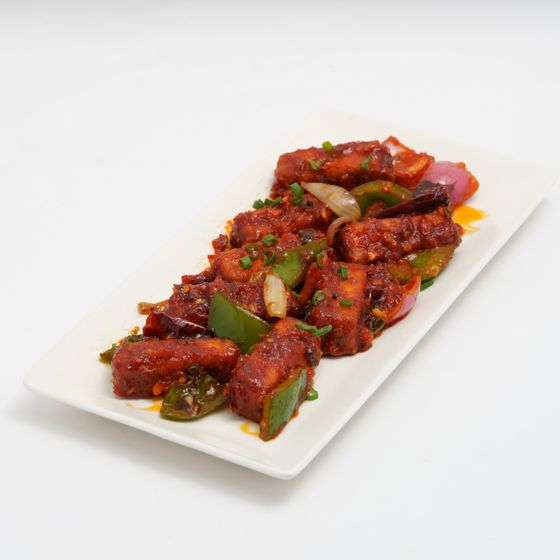 Crispy paneer in sticky red chili sauce with green pepper and onion on a platter