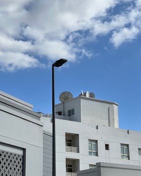 White buildings with satellite dishes and a streetlamp in Dubai against a bright blue sky.