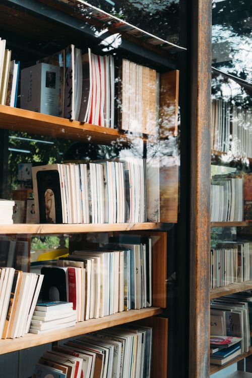Free Books neatly arranged on a wooden bookshelf reflecting a serene outdoor view in Guangxi, China. Stock Photo