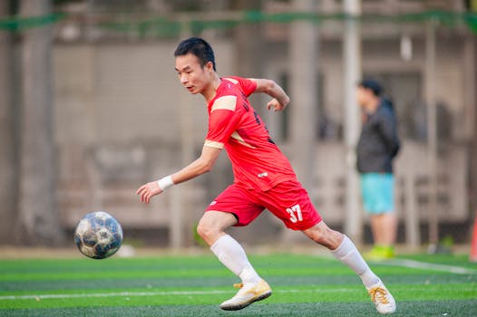 Male soccer player in red uniform playing on a grass field in Hanoi, Vietnam.