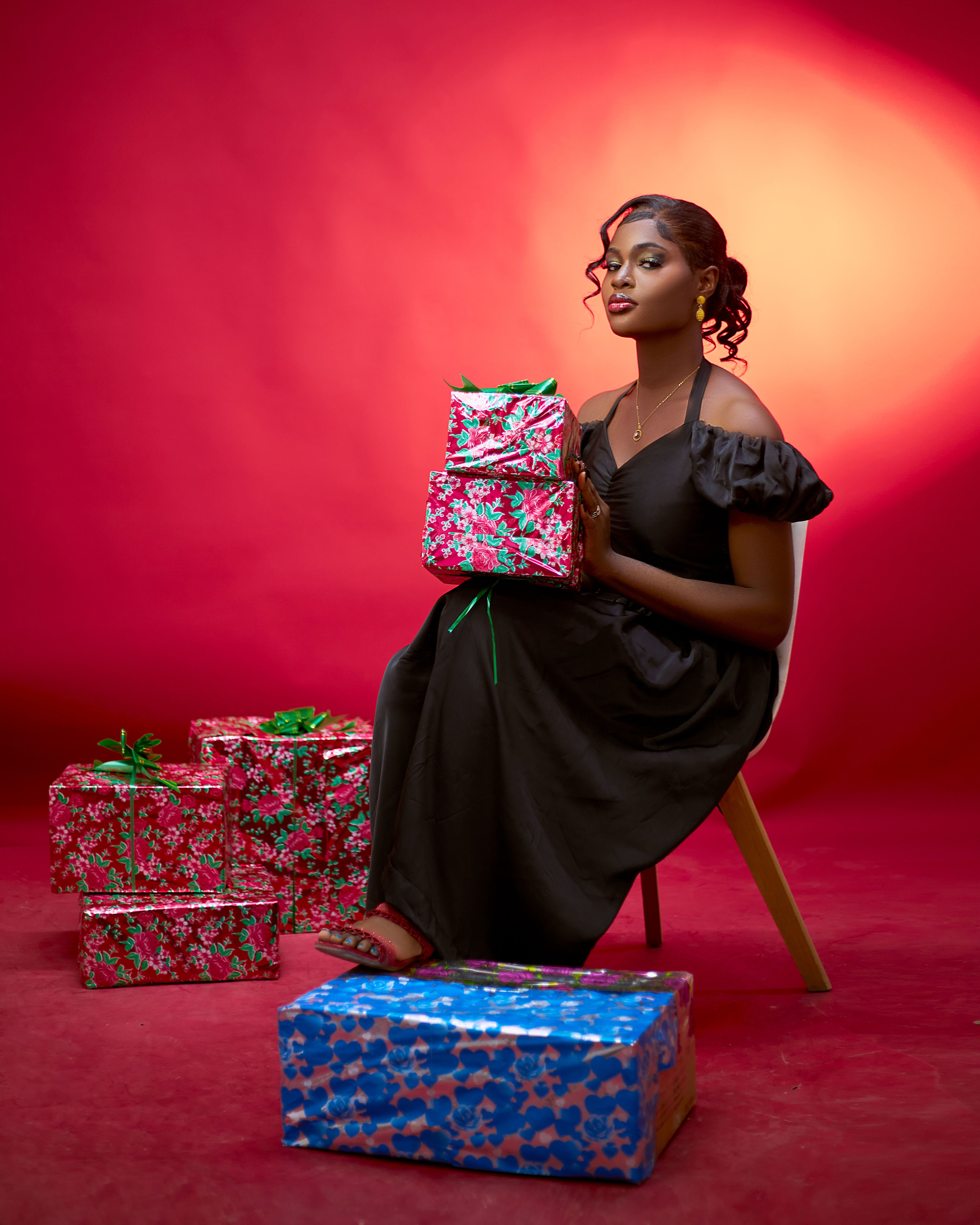 Graceful woman in black dress holding colorful gifts with a red background, festive and elegant.