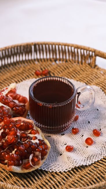 A warm cup of pomegranate tea with fresh seeds on a wicker basket.