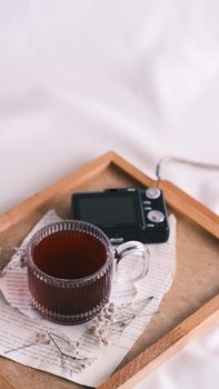 A warm cup of tea placed on a wooden tray with an old film camera and dried flowers.