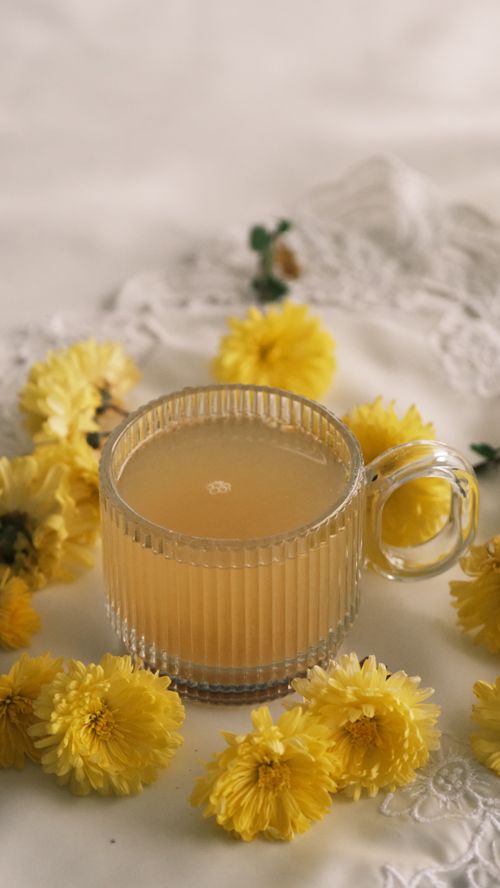 Free A delicate glass cup filled with chamomile tea surrounded by yellow flowers on a lace cloth. Stock Photo