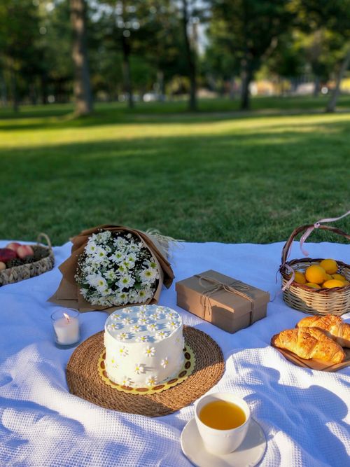 Free Inviting picnic setup with cake, flowers, and treats on a sunny day. Stock Photo