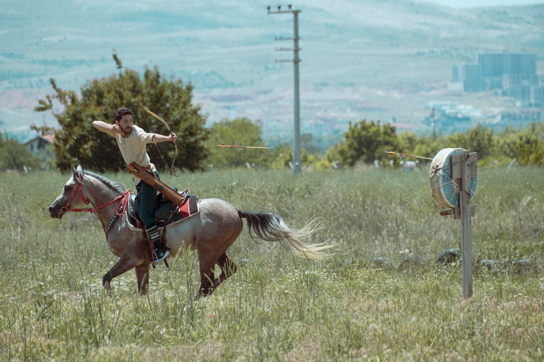 Dynamic scene of a mounted archer practicing in a field with a clear mountain backdrop in Konya, Türkiye. Captured outdoors in daylight.
