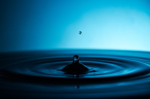 Free A lone water droplet creates ripples against a calming blue background. Stock Photo