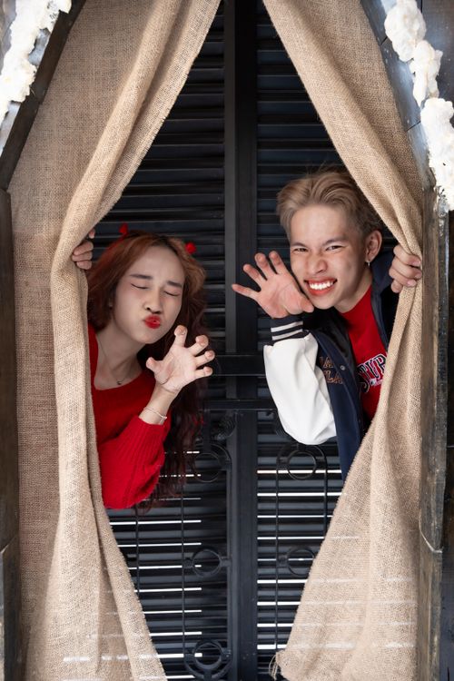 Free Two young adults playfully pose behind burlap curtains indoors. Stock Photo