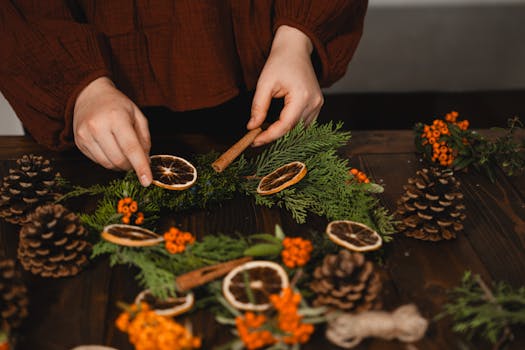 Hands decorating a Christmas wreath with dried oranges and pinecones.